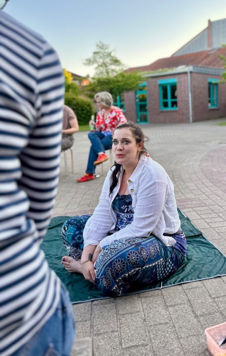 Frau sitzend, draußen auf dem Boden ins Gespräch vertieft